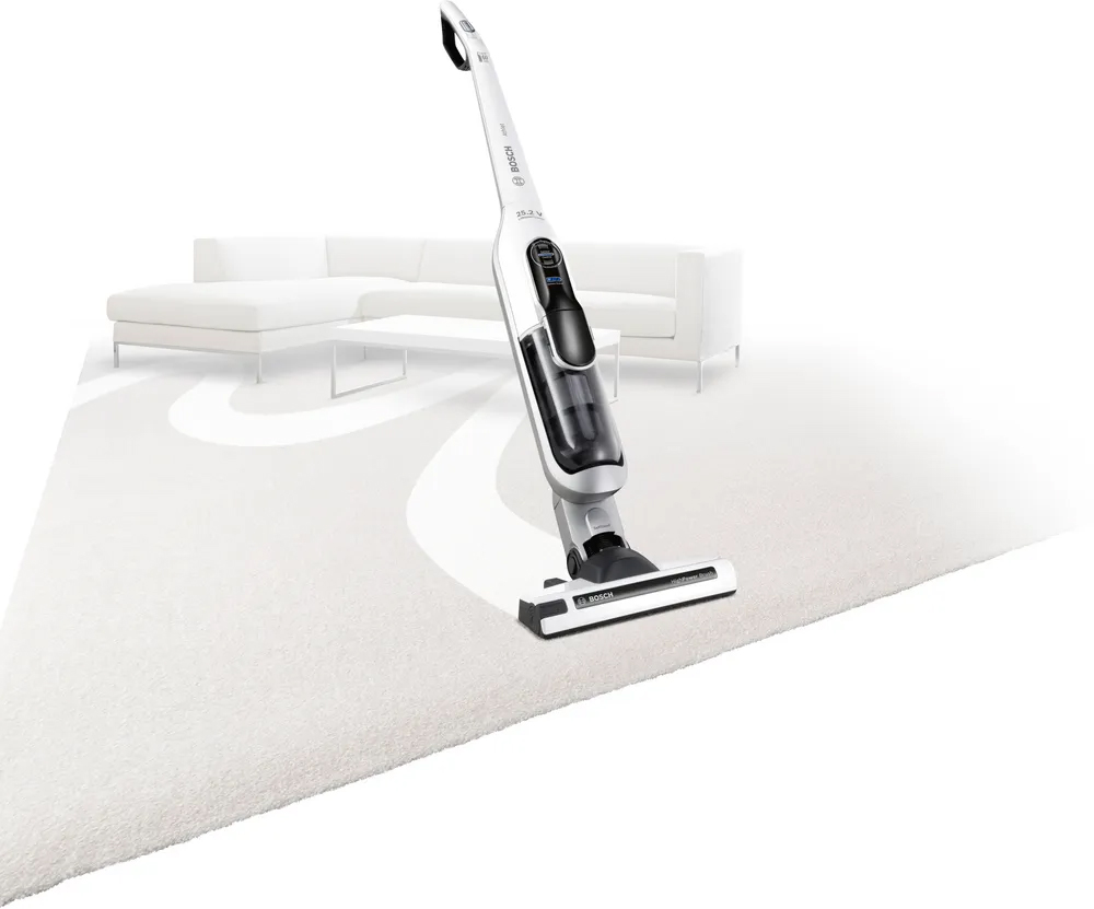 Απεικονίζεται η σκούπα να σκουπίζει ένα χαλί. Πίσω φαίνεται ένας λευκός καναπές.